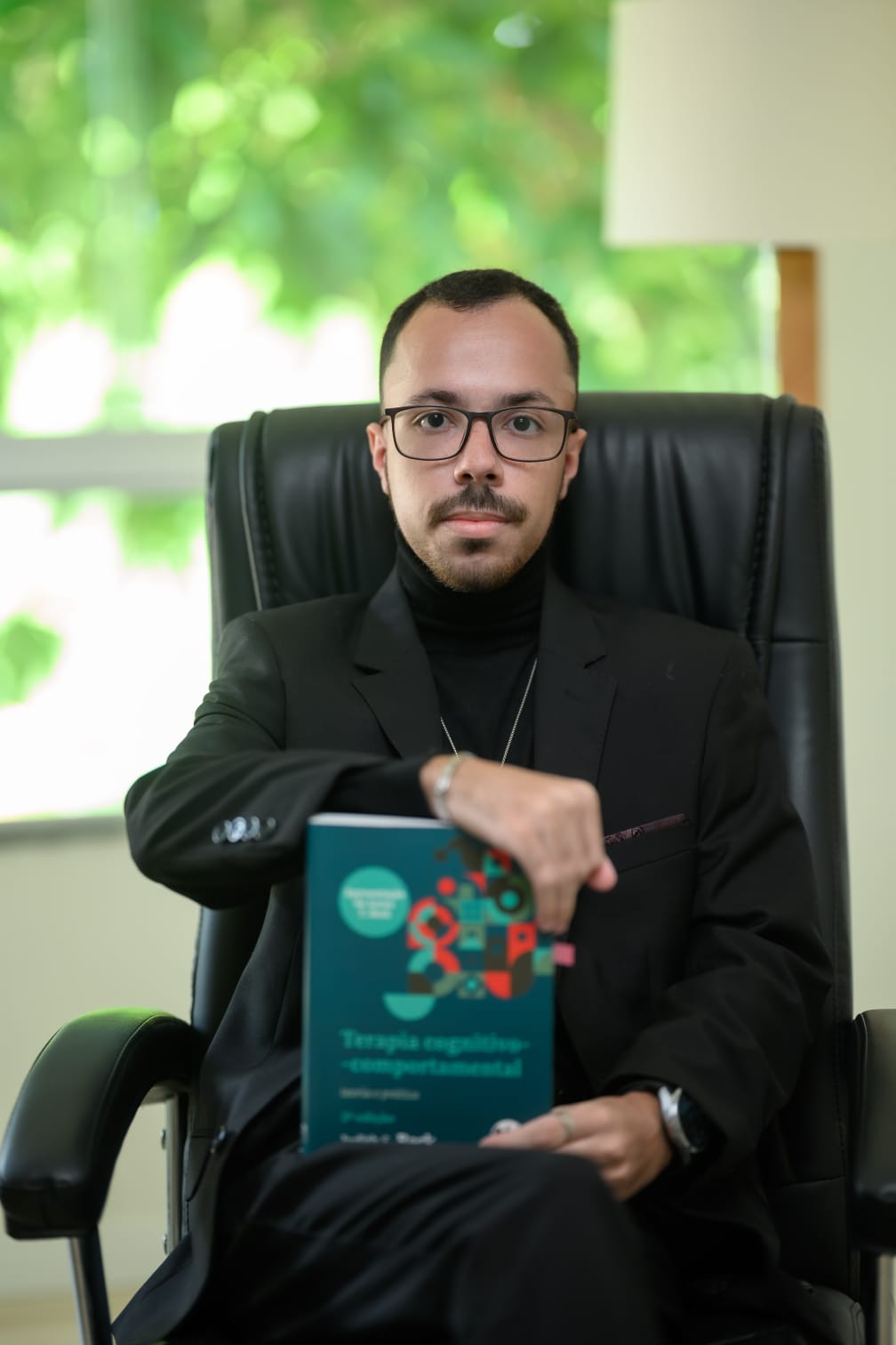 Caio sentado segurando um livro de Terapia Cognitivo-Comportamental
